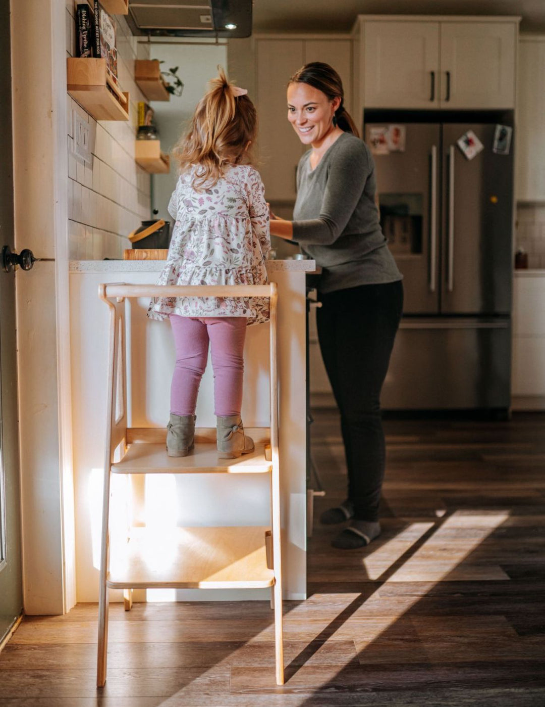 toddler standing on a toddler tower helping the mother in the kitchen